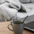 grey laptop on desk with cup of coffee in front of a sofa. working from home concept