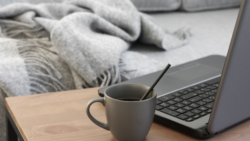 grey laptop on desk with cup of coffee in front of a sofa. working from home concept